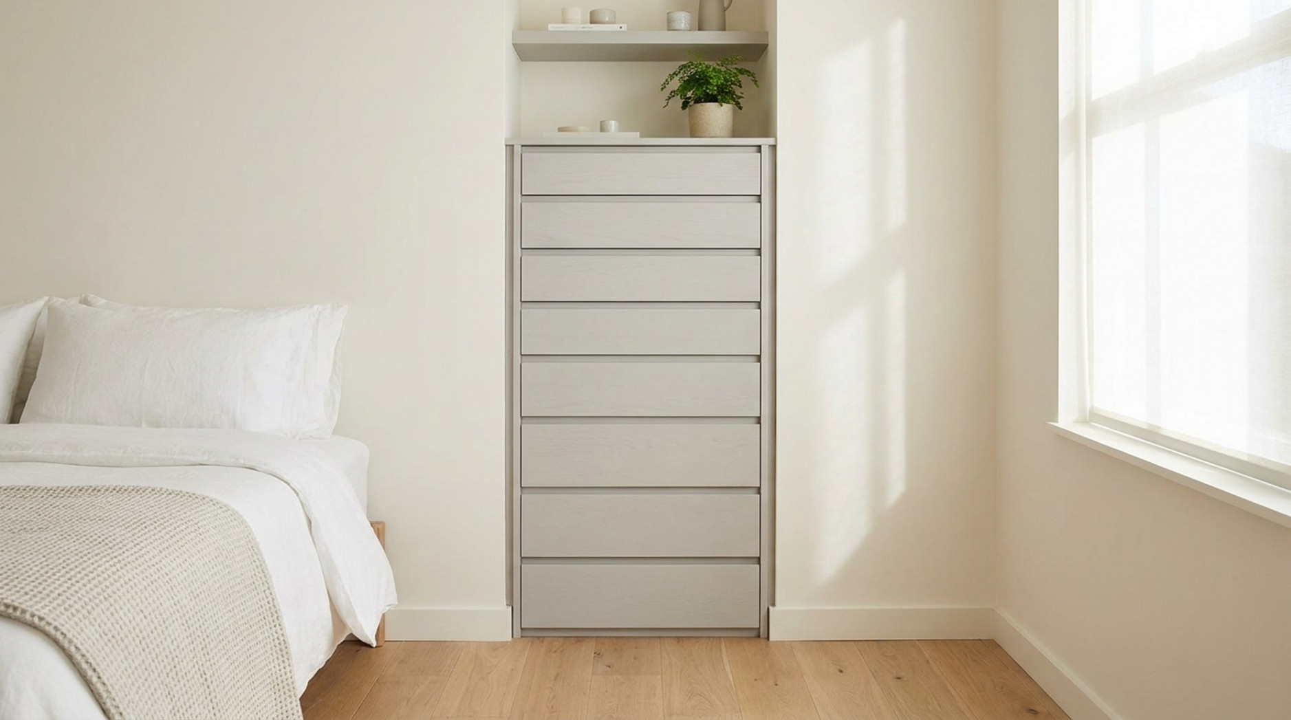 Schmale hohe Kommode mit mehreren Schubladen in einem hellen Schlafzimmer neben Bett und Fenster