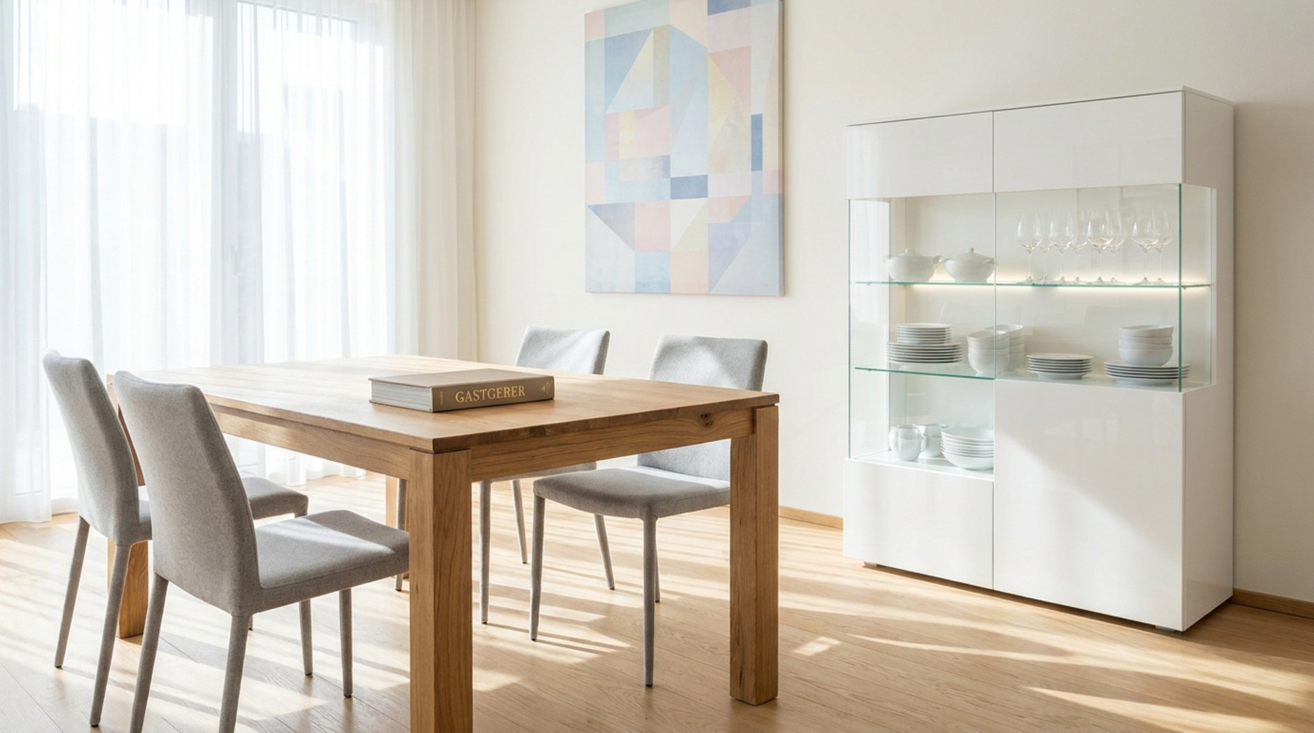 Weiße Vitrine mit Glasfront, Geschirr und Weingläsern neben einem Holzesstisch mit grauen Stühlen